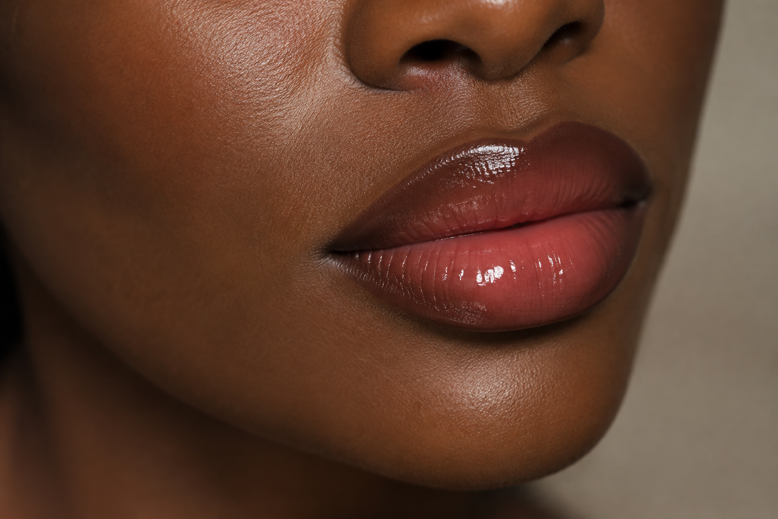 Close-up of a woman with deep dark skin wearing defined brown lip liner, rose-brown lip color, and clear gloss.