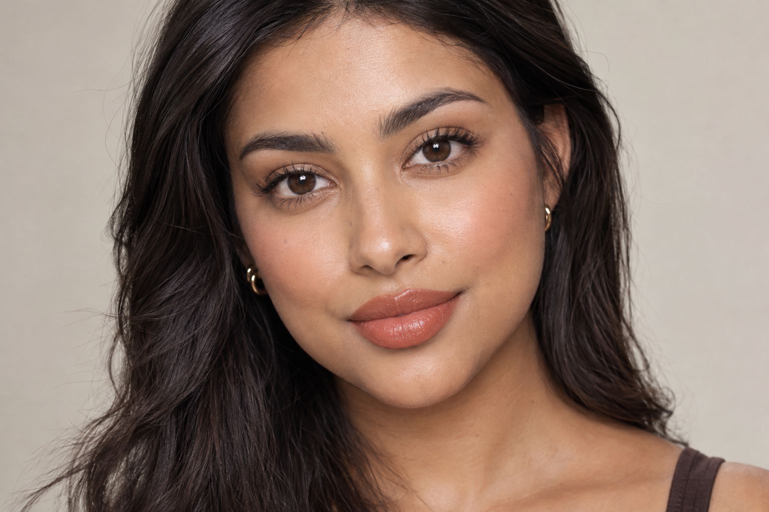 Woman with medium skin wearing peach-brown satin lipstick and understated eye and cheek makeup.