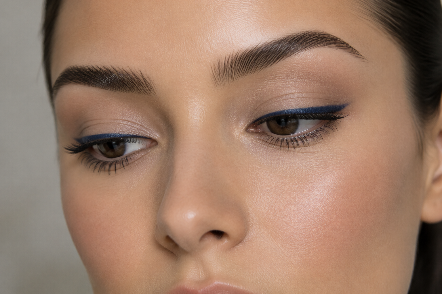 Close view of a woman with brown eyes wearing sheer taupe eyeshadow and narrow navy upper-lash liner that thickens slightly at the outer corners.