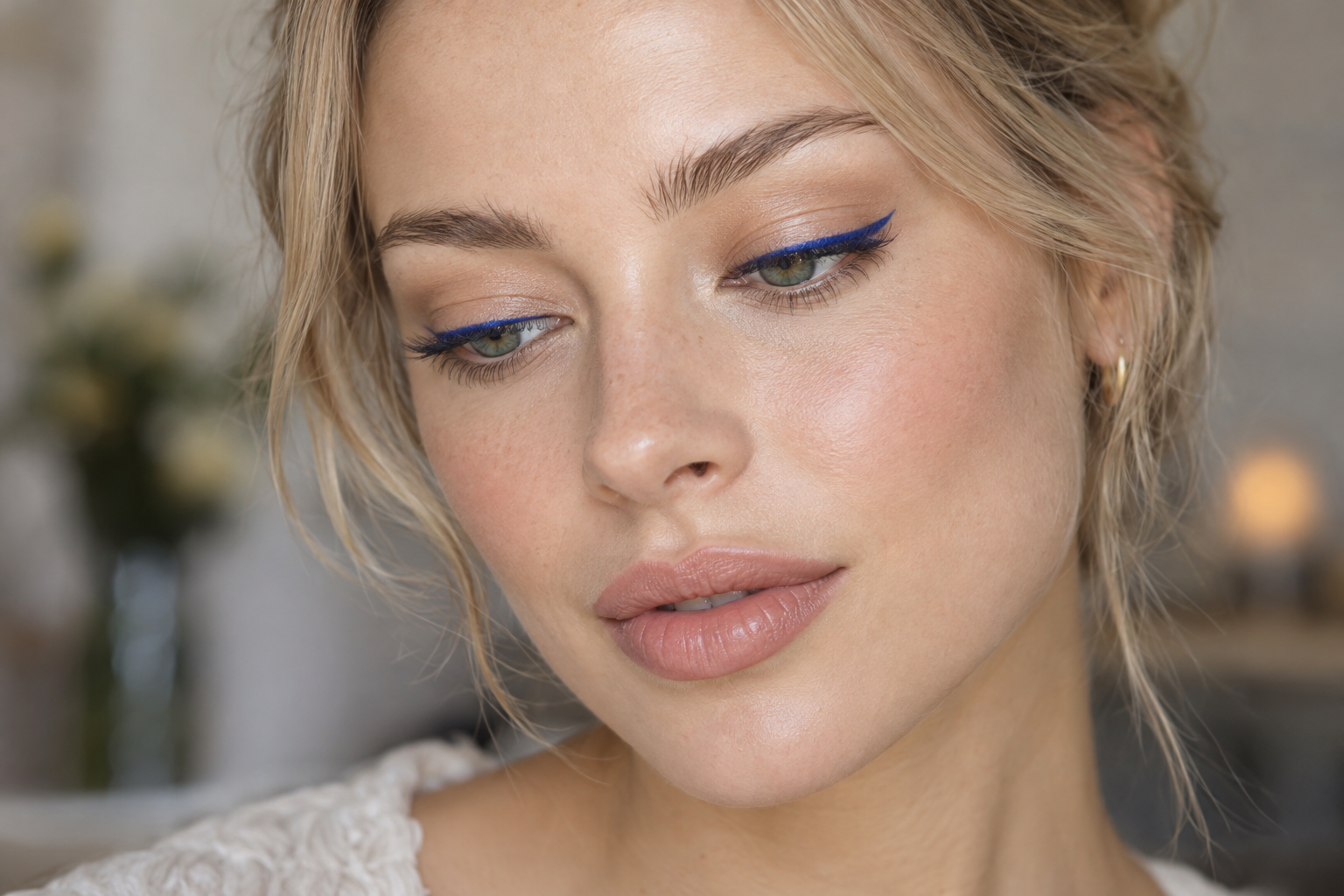 Sandy-blonde woman with softly lowered green eyes wearing narrow cobalt-blue eyeliner along her upper lashes and neutral lip color.